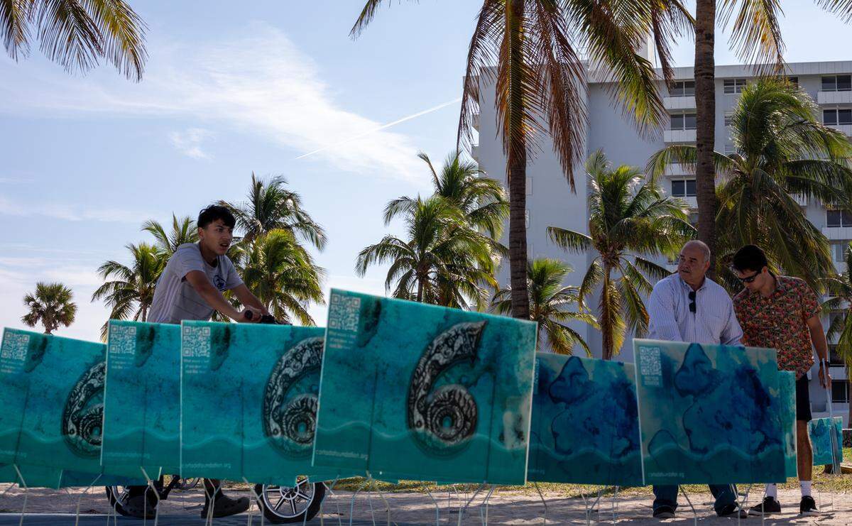 A biker passes by the yard signs Xavier Cortada installed in a progression at Sandy’s Beach in Miami Beach on Monday, Dec. 6.