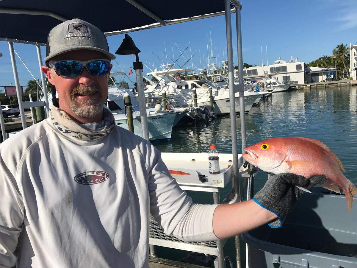 Mike Ondrasek, a charter fishing boat mate in Islamorada, holds a yelloweye snapper at the cleaning table of the Postcard Inn Resort and Marina Thursday, March 12, 2020.