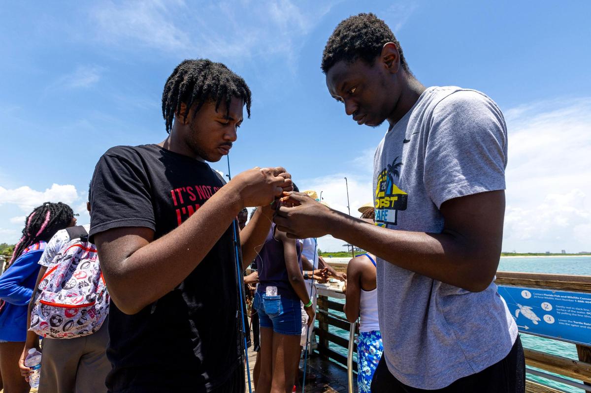 Campers Alex Baptise and Giovanny Desire bait a hook during a Root Collective’s summer camp field trip at Dania Beach Pier in Dania Beach.