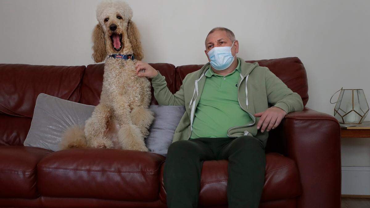 In this file photo, long COVID patient Gary Miller sits on his sofa at home with his dog Rupert in London, Tuesday, May 11, 2021. For taxi driver Miller, recovery is agonizingly slow.