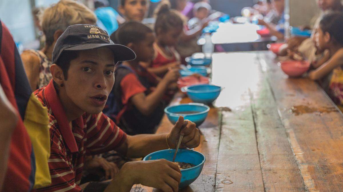 Young, elderly and disabled Venezuelans all squeeze in together in the dining room of Casa de Maria in Propatria to eat a bowl of soup.