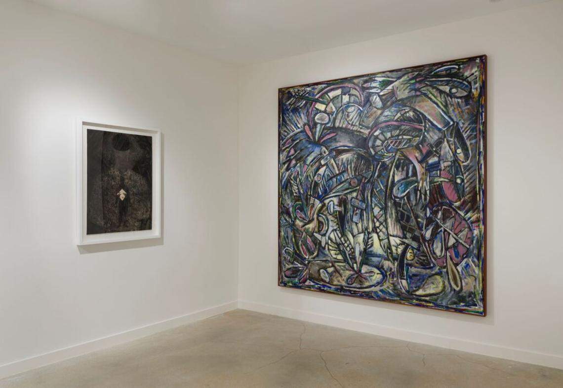 A painting by Alfonzo,”Thirst,” next to a print by Ayón depicting a woman removing a mask. Alfonzo’s painting exemplifies his darker later work from the time before he died of complications from AIDS.