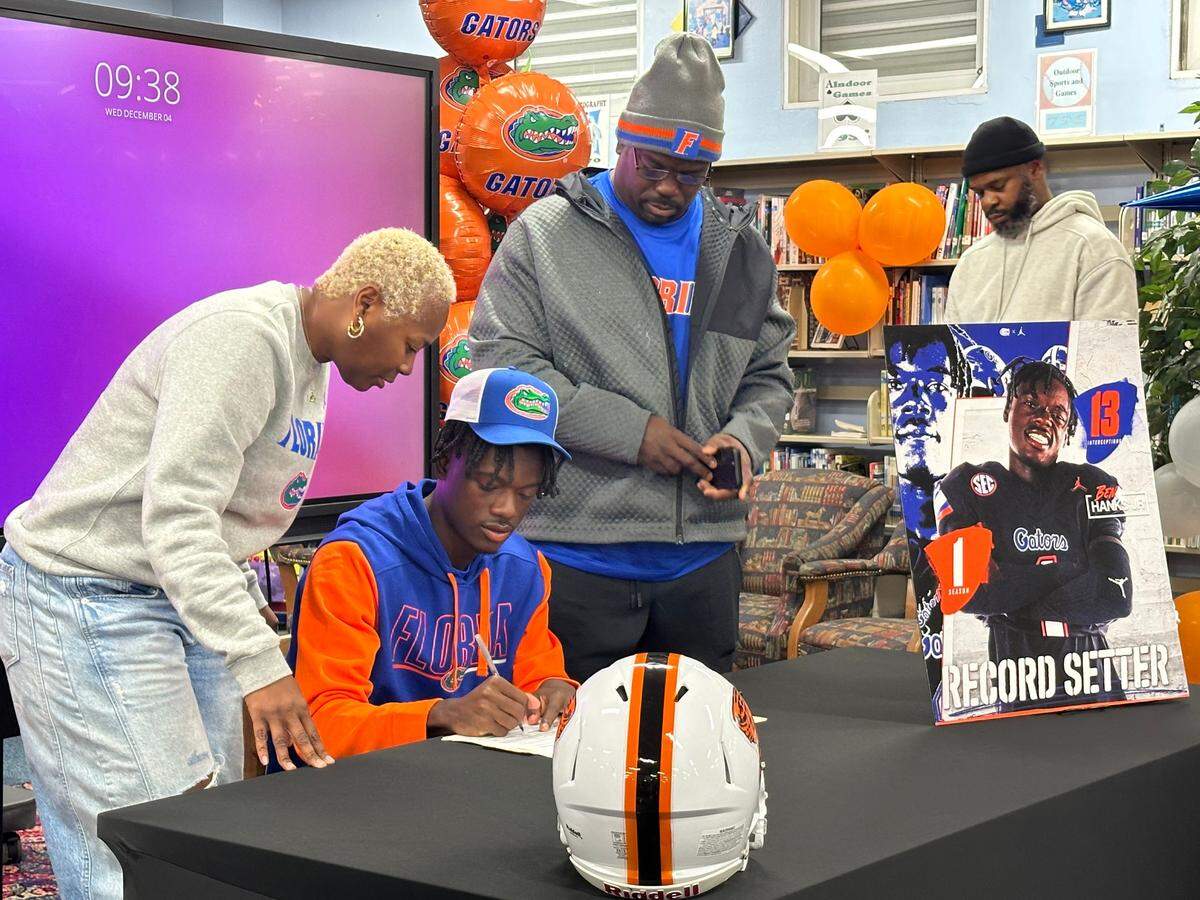 Miami Booker T. Washington’s Ben Hanks III signs his letter of intent with the University of Florida on Wednesday, Dec. 4, 2024 with his parents at his side during a ceremony at Booker T. Washington High School in Miami, Fla.