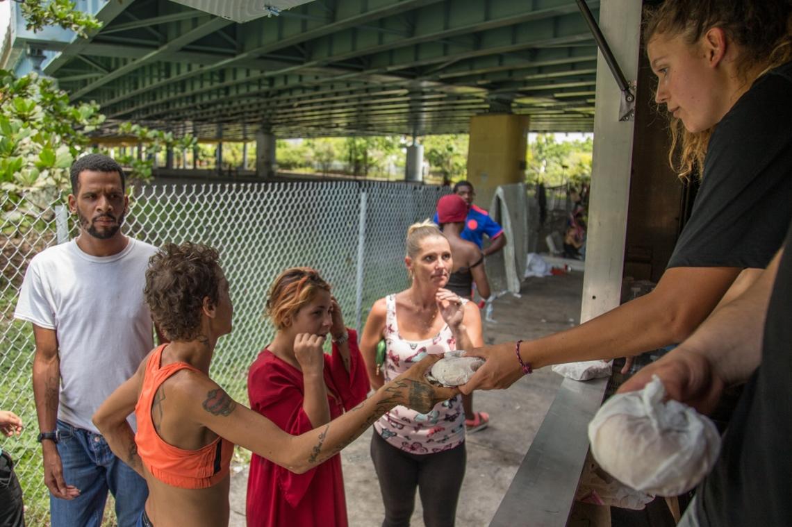 University of Miami student athlete Hannah Marwede, right, gives out food and water to those in need from the Second Spoon food truck in the neighborhood of Overtown in Miami where many homeless people stay under Interstate 395 on Saturday, July 7, 2018.