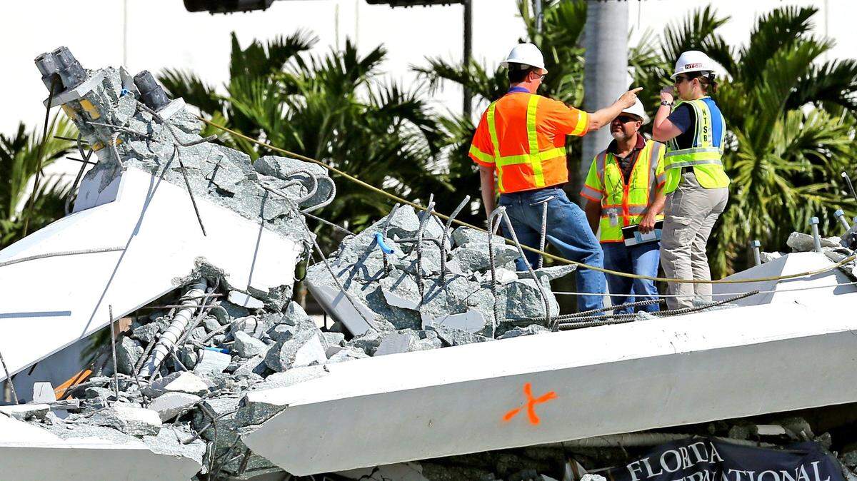 On March 16, 2018, National Transportation Safety Board inspectors stand along a section of the FIU bridge. The bridge collapsed a day earlier on cars that were traveling along the roadway. Six people were killed.
