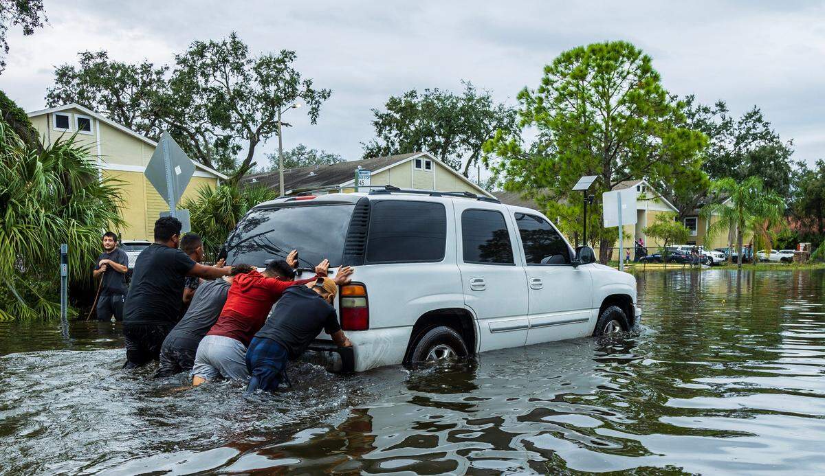 A group of men pushed a broken down SUV through the flooded N 12th St in North Tampa, Thursday, October 10, 2024, a day after Hurricane Milton crossed Florida’s Gulf Coast.