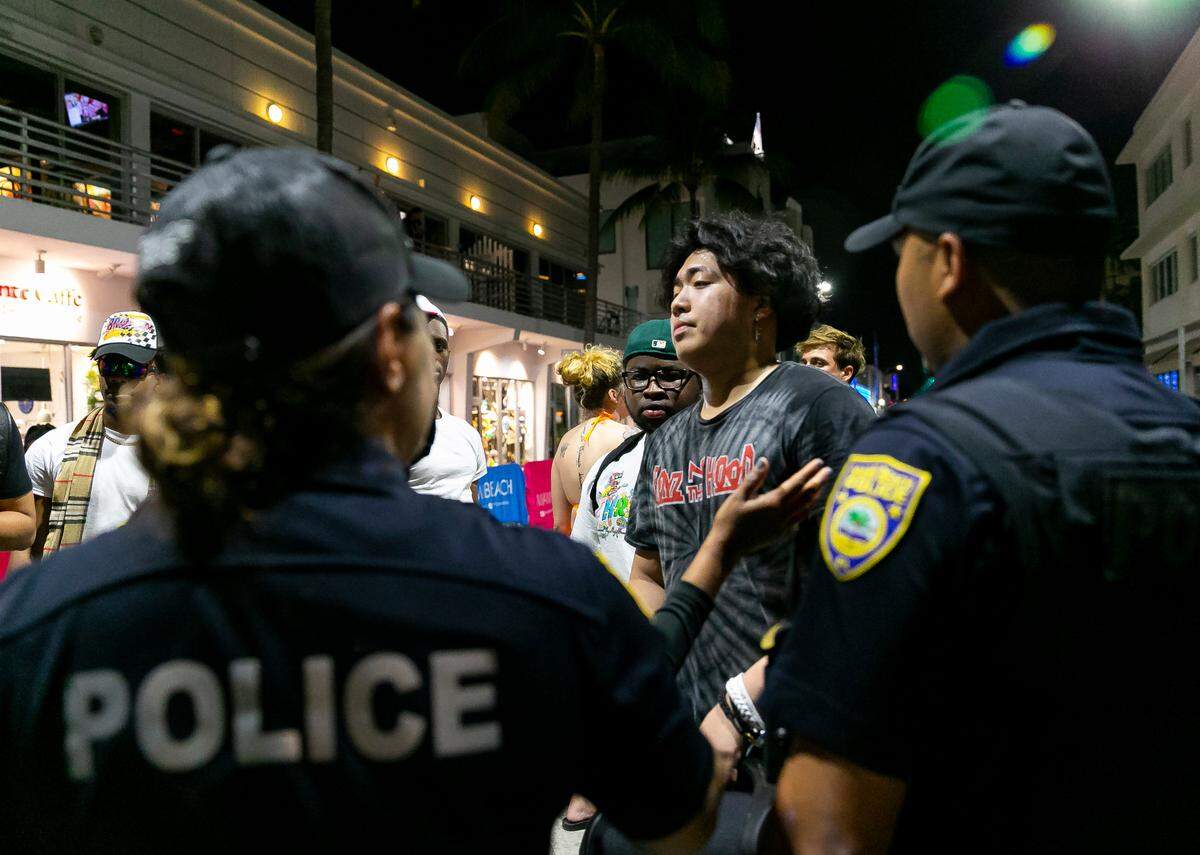 Police officers force TikToker Jodey De Los Santos, center, and other social media influencers to stop filming videos on Ocean Drive and 8th Street in Miami Beach, Florida on Friday, March 25, 2022. City officials imposed a midnight curfew and forced stores to stop selling alcohol after 6 p.m. The restrictions were set in place after two shootings in Miami Beach the weekend before caused city officials to announce a “state of emergency.”