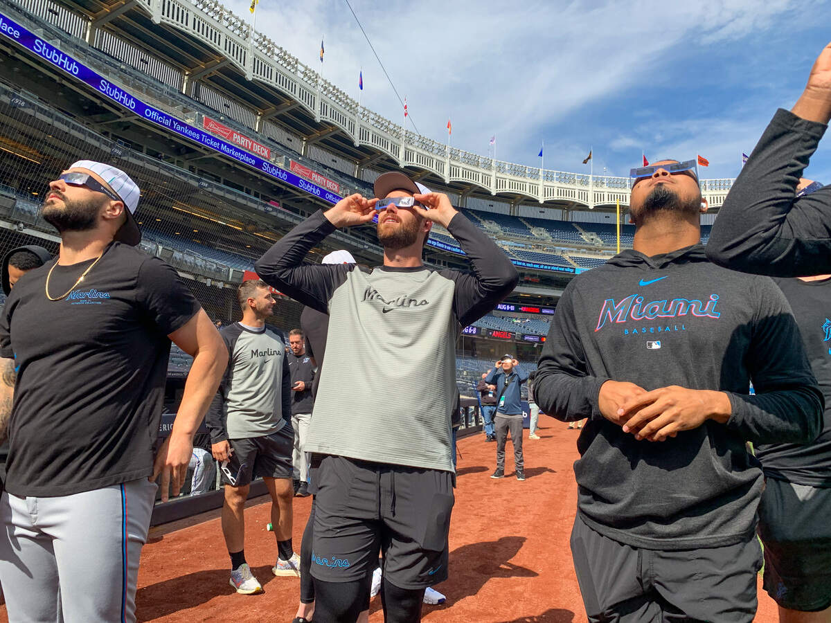 Miami Marlins players Tanner Scott, Anthony Bender and Luis Arraez look up at the sky to watch the solar eclipse on Monday, April 8, 2024, from the field at Yankee Stadium.