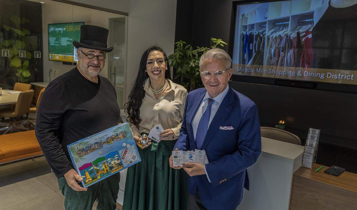 From left- Eddy Martinez, owner of the BLISS Imprints & Gifts store, Cristina Miller, President of the Coral Gables Foundation and Jorge L. Arrizurieta, President of the Coral Gables Chamber of Commerce,  posed holding  cards and banner of the Gables-Opoly, a Coral Gables-themed Monopoly-style game, during a meeting at the Coral Gables Chamber of Commerce, on Tuesday, March 17, 2026.