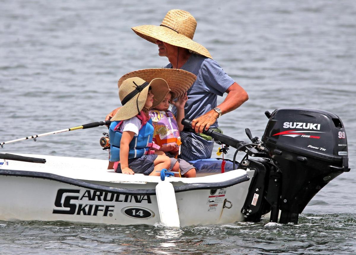 A fisherman with two girls, all wearing wide brim hats to shade from the sun, go fishing near the Haulover sandbar in Miami-Dade, Florida, June 21, 2021.