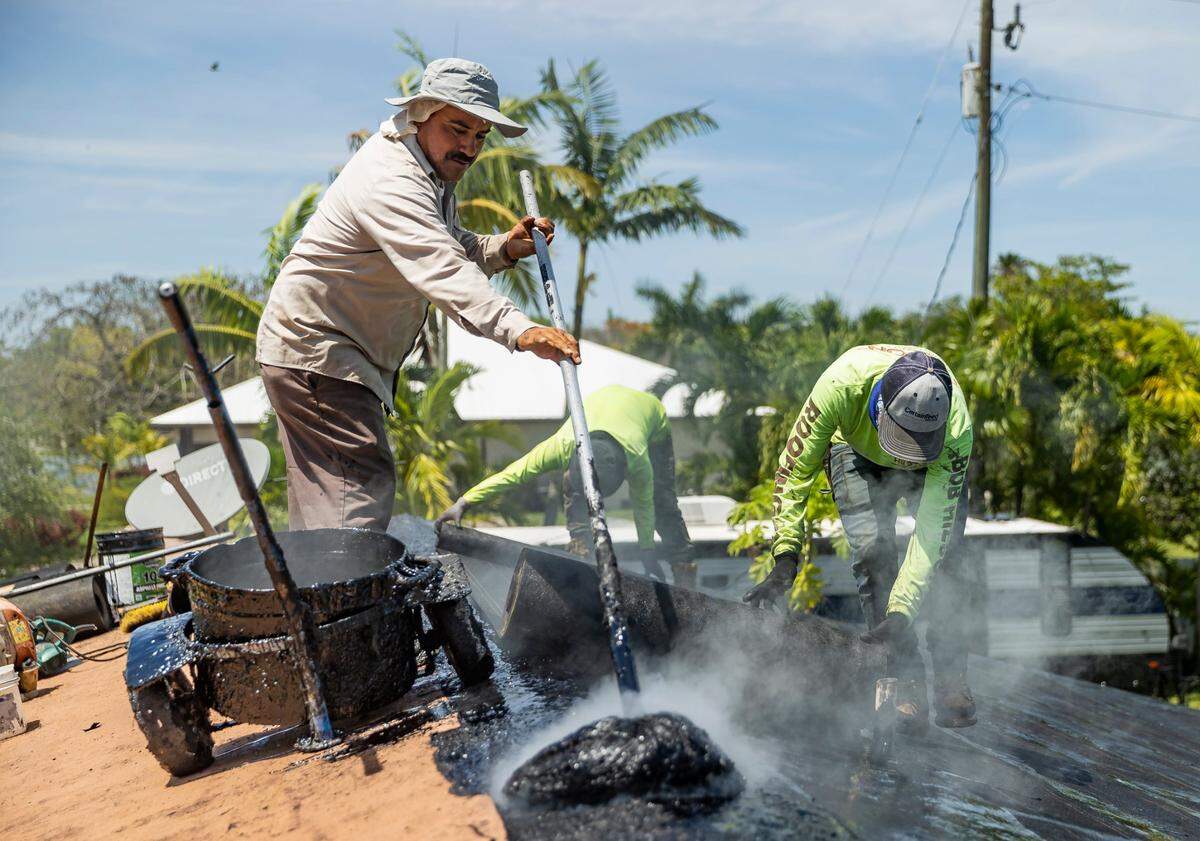 Gilberto Lujano, de 49 años, a la izquierda, esparce alquitrán mientras trabaja en un tejado el martes 2 de mayo de 2023, en Homestead, Florida.