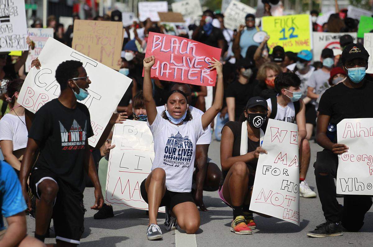 South Florida protesters hold up signs while on one knee as part of demonstrations in reaction to the death of George Floyd, who died in police custody in Minneapolis on May 25, after a police officer pressed a knee against Floyd’s neck for nearly nine minutes .