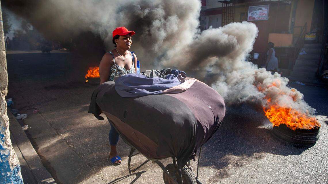 A woman pushes her merchandise away from tires set on fire by protesters during a countrywide strike demanding the resignation of Haitian President Jovenel Moise in Port-au-Prince, Haiti, Monday, Feb. 1, 2021. Opposition leaders are pushing for Moïse to step down on Feb. 7, while Moïse has said his term ends in February 2022.