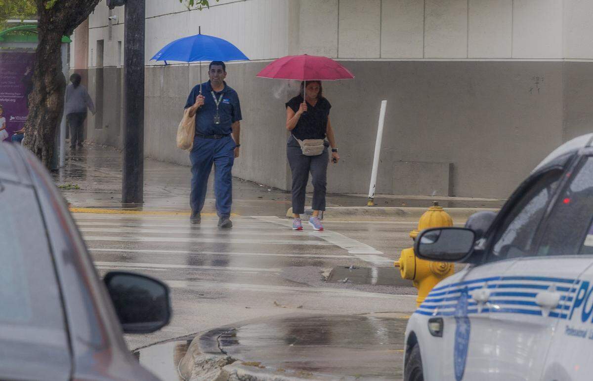 A couple take cover under an umbrella as they walk along NW 2nd Ave, during a cloudy morning as the National Weather Service predicts rain chances near 50%, during the afternoon, on Wednesday, March 18, 2026.