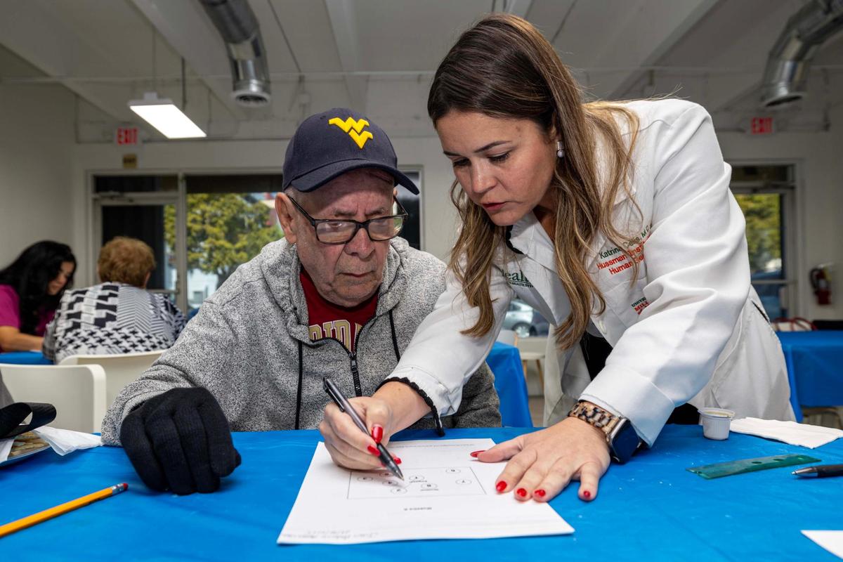 La investigadora médica de UHealth, la Dra. Katrina Celis, (derecha), realiza una prueba como parte de un estudio sobre el Alzheimer en Juan Antonio Ascasio Vedo, durante un evento de extensión comunitariad el Instituto John P. Hussman de Genómica Humana, donde los investigadores de UM realizaron pruebas, inscribieron a nuevos participantes y llevaron muestras de sangre a un nuevo biorrepositorio que se inauguró en el campus de UHealth el jueves 16 de enero de 2025, en Hialeah, Florida.