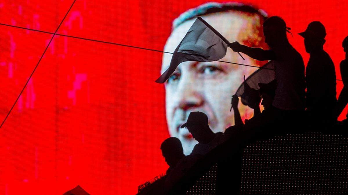 People wave Turkish flags in front of an electronic image of President Recep Tayyip Erdogan, who now runs a virtual dictatorship.