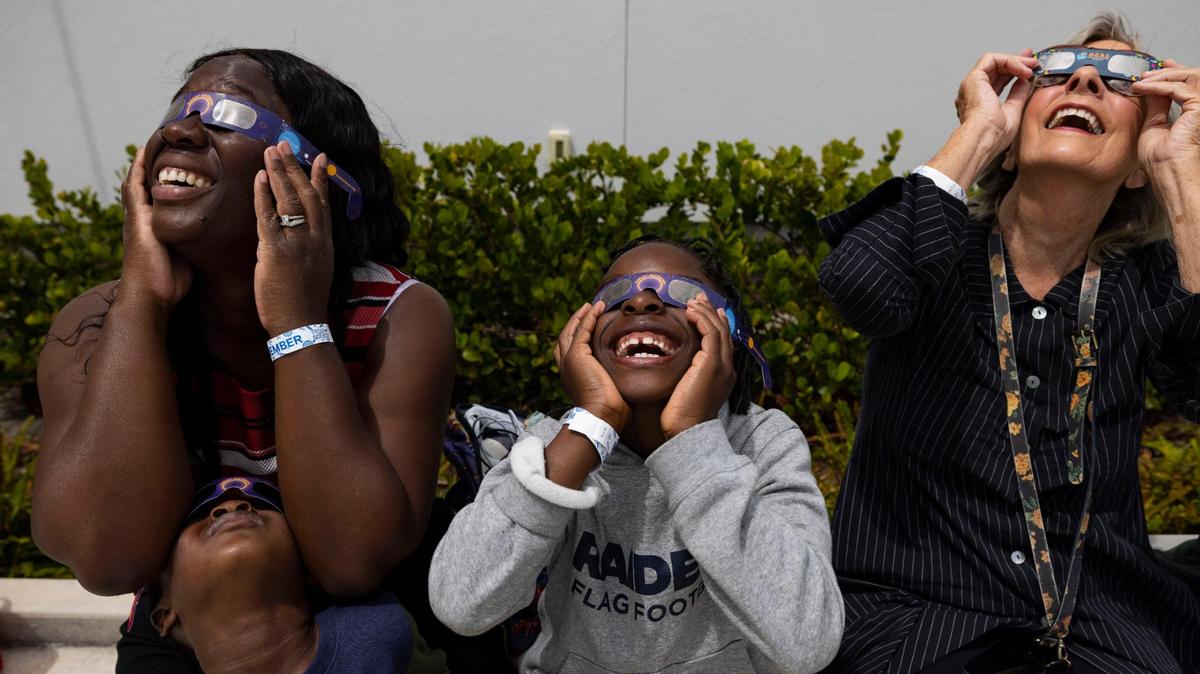 Nathalie Blanfort, left, and her sons, Noah, 4, and Bryson, 6, watch the solar eclipse with Doris Ugarriza, right, on the roof of the museum on Monday, April 8, 2024, at The Phillip and Patricia Frost Museum of Science in downtown Miami. “Oh my gosh it’s happening!!” said Bryson, center.