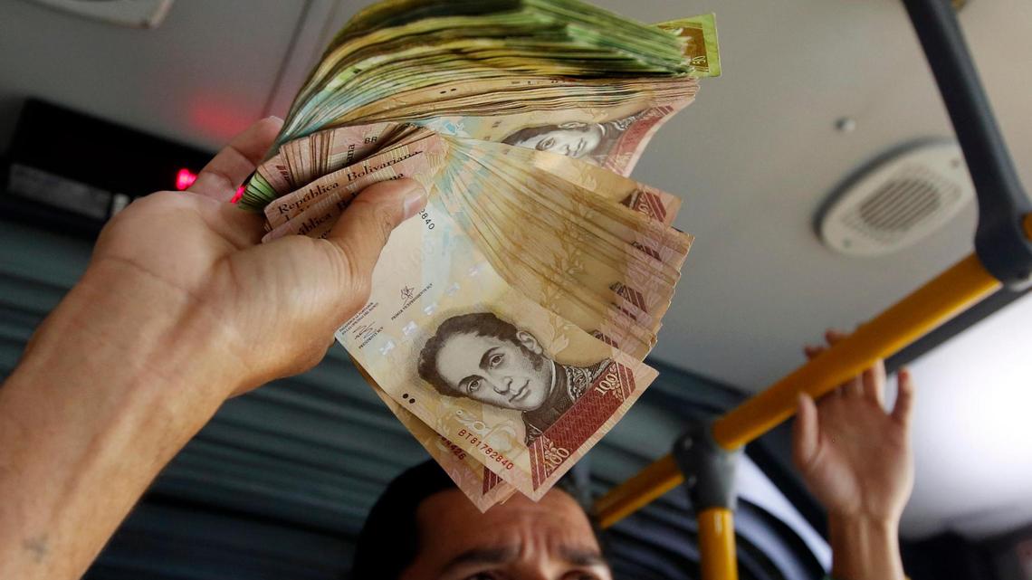 In this Dec. 12, 2017 file photo, Venezuelan national Jorge Gutierrez holds a wad of Venezuelan bolivars that he wanted to exchange for some Colombian money, as he rode a bus in Bogota, Colombia. Venezuela was abandoning the most-overvalued of its two official foreign exchange rates, which had been used for state imports of food and medicine amid a worsening economic crisis. The exchange rate reforms became public Monday, Jan. 29, 2018.