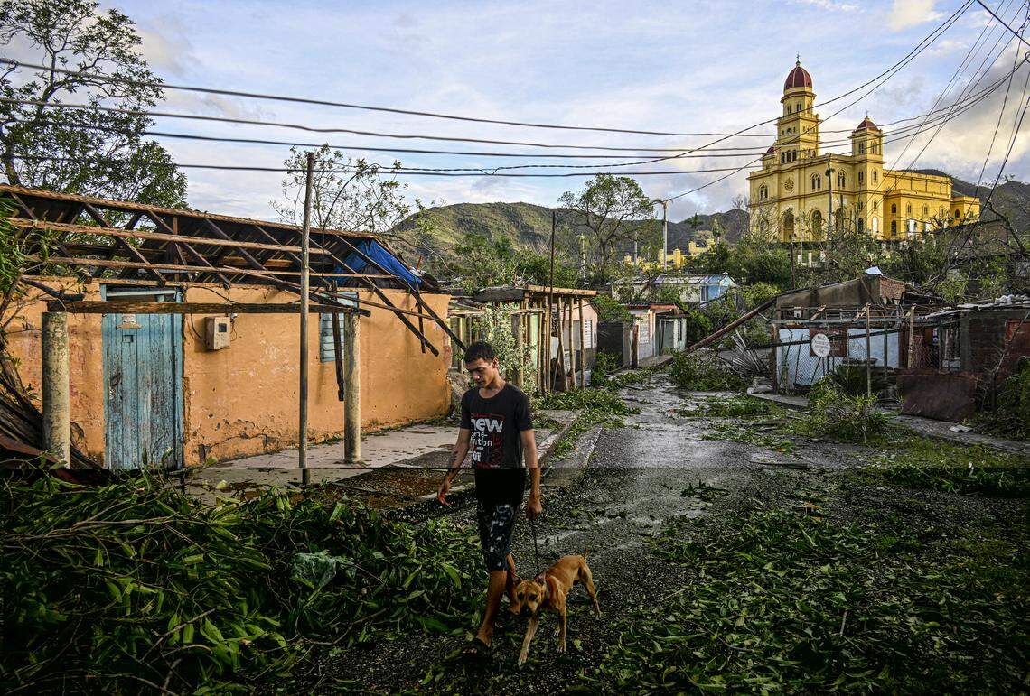 A resident of El Cobre, in the province of Santiago de Cuba, walks his dog past downed trees, power lines and destroyed houses following the passage of Hurricane Melissa, on October 29, 2025.    