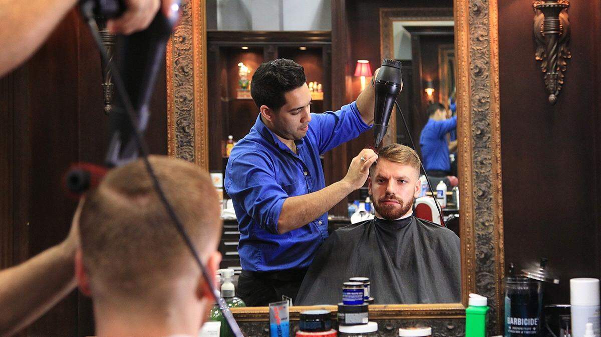El barbero de Churchill’s, Julian Fernández, a la izquierda, le seca el cabello a su cliente, Vlad Mihai, de 26 años, un camarero en South Beach, el miércoles 27 de enero de 2016.