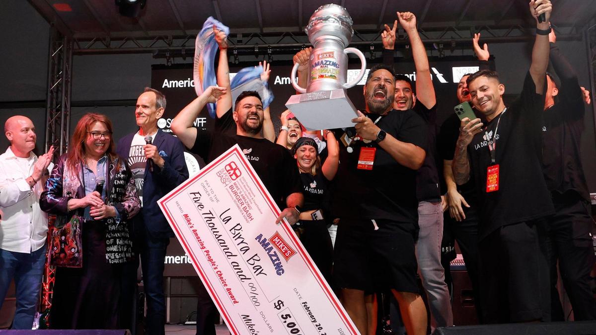 Renzo Cocchia, co-owner of La Birra Bar, holds a check and celebrates with his team on stage at Burger Bash 2025 after winning the People’s Choice Award. Host Rachael Ray is at left.