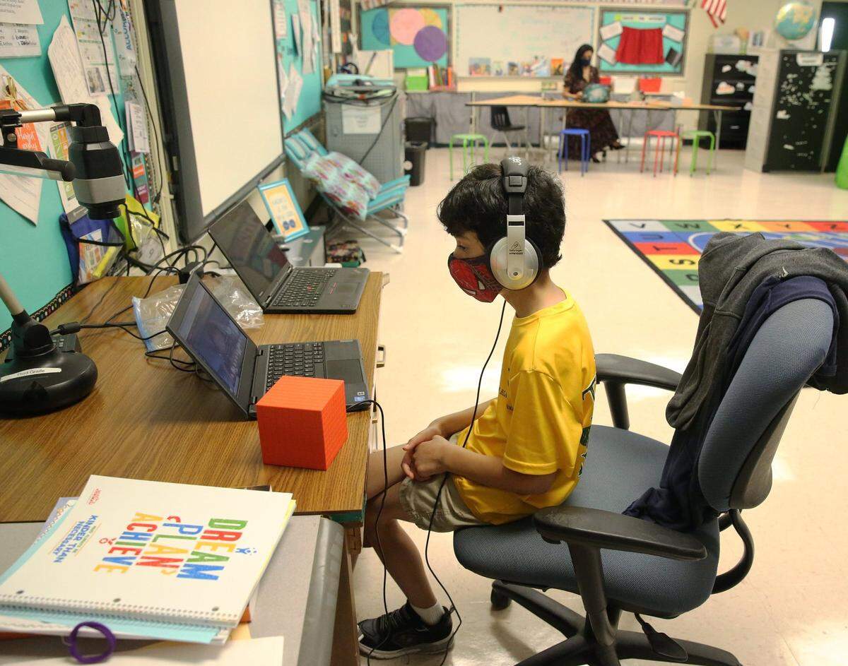 La maestra de la escuela primaria Nova Blanche Forman, Attiya Batool, enseña su clase de cuarto grado virtualmente mientras su hijo, Nabeel, hace su trabajo de clase de segundo grado en línea en su aula de Davie durante el primer día de clases en Broward, el 19 de agosto. Todas las clases en las escuelas públicas de Broward se están enseñando de forma remota. El distrito escolar ha permitido que algunos maestros lleven a sus hijos a su salón de clases para que asistan a clases remotas mientras enseñan.