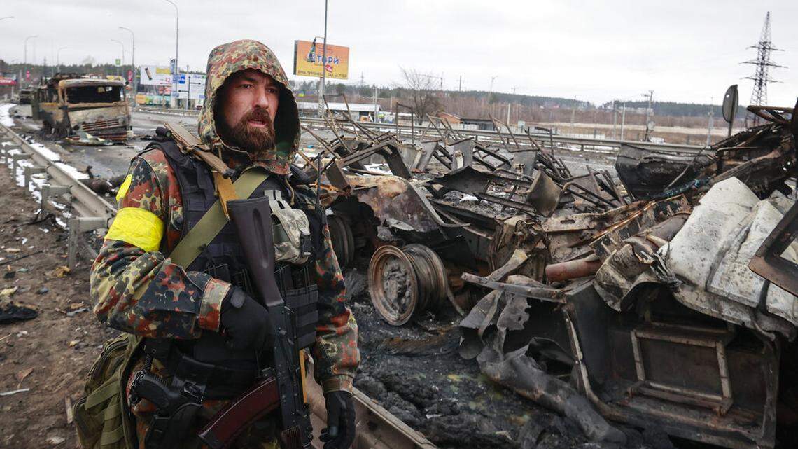 An armed man stands by the remains of a Russian military vehicle in Bucha, close to the capital Kyiv, Ukraine, Tuesday, March 1, 2022.