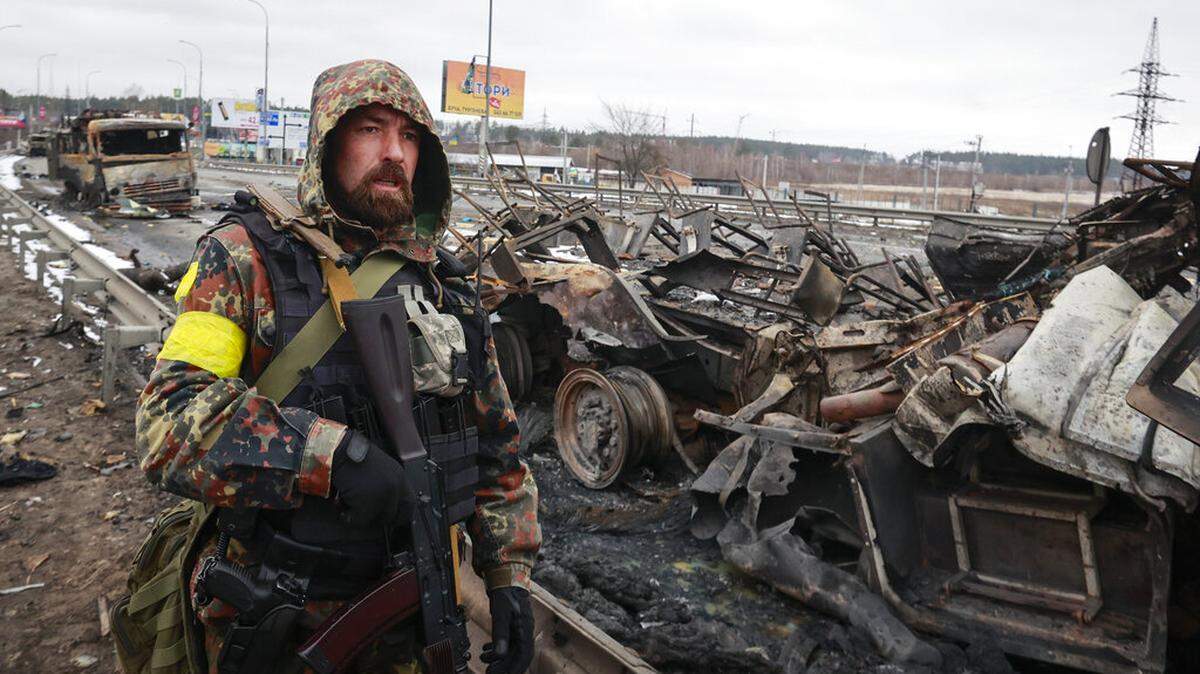 An armed man stands by the remains of a Russian military vehicle in Bucha, close to the capital Kyiv, Ukraine, Tuesday, March 1, 2022.