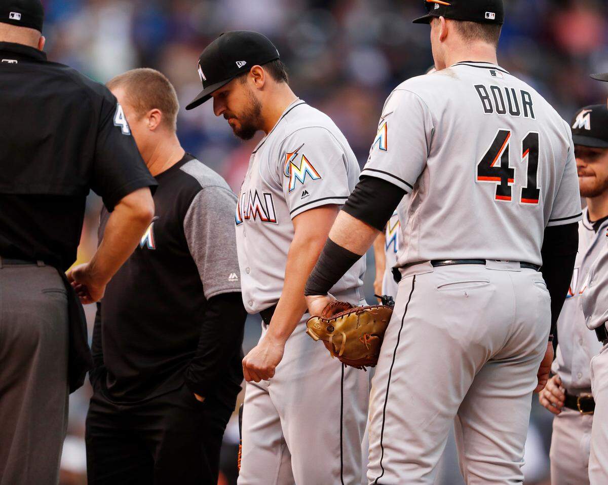 Miami Marlins starting pitcher Caleb Smith, center, is pulled from the mound after being checked for an injury in the second inning of a baseball game against the Colorado Rockies Sunday, June 24, 2018, in Denver. (AP Photo/David Zalubowski)