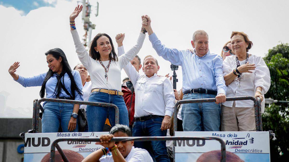 María Corina Machado (M, izq.), líder opositora, y Edmundo González Urrutia (M, der.), candidato presidencial opositor, levantan los puños mientras conducen un automóvil en una manifestación contra los resultados oficiales de las elecciones presidenciales en julio de 2024.