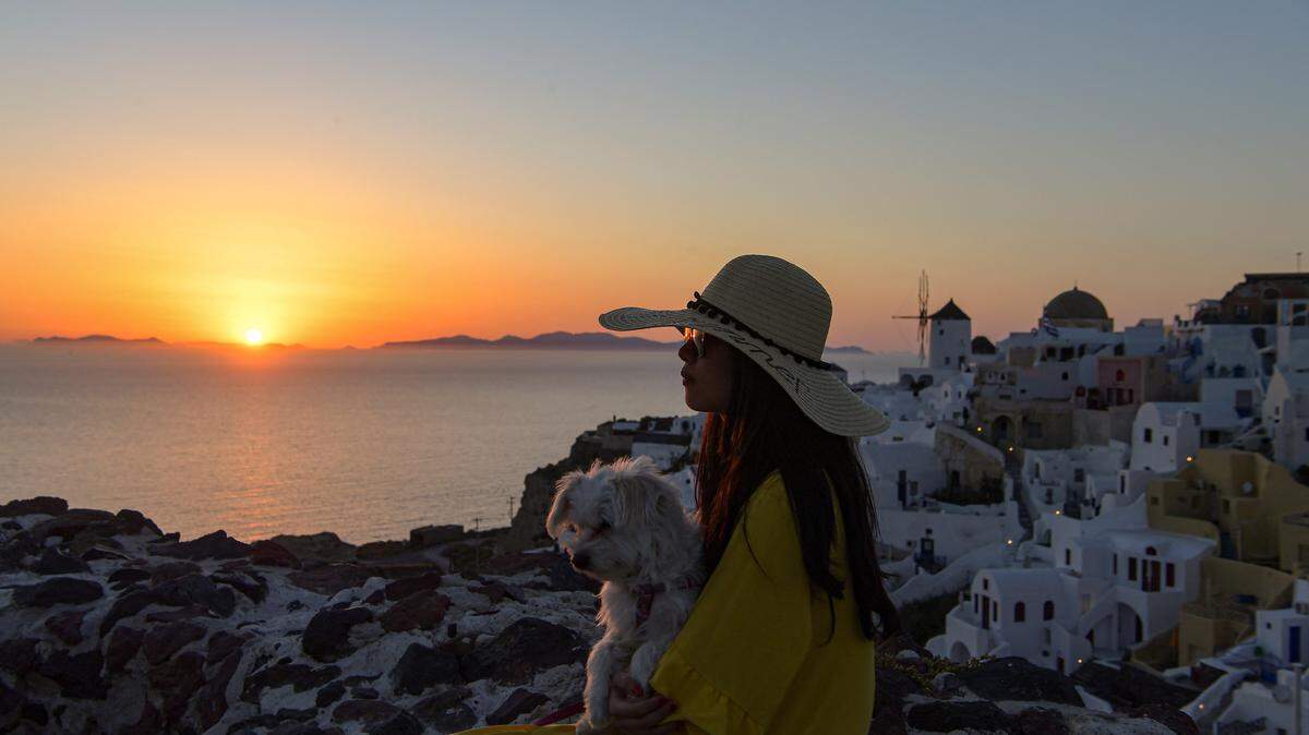 A woman sits with her dog as she looks at the sunset in the town of Oia in the island of Santorini on June 14, 2020.