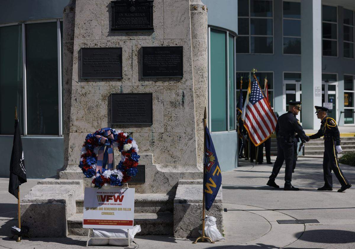 Two officers shake hands to the right of the Memorial Day wreath sponsored by the Veterans of Foreign Wars 3559 Miami Beach Post during a Memorial Day Commemoration on Monday, May 25, 2026, at Miami Beach Police Headquarters in Miami Beach, Fla. 