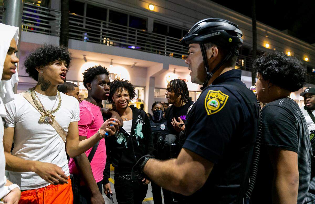 A police officer talks with social media influencers forcing them to stop filming videos on Ocean Drive and 8th Street in Miami Beach, Florida on Friday, March 25, 2022. City officials imposed a midnight curfew and forced stores to stop selling alcohol after 6 p.m. The restrictions were set in place after two shootings in Miami Beach the weekend before caused city officials to announce a “state of emergency.”