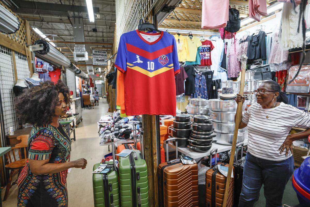Enam Ayee, at left, speaks with Lisa Gean, at right, about the Haitian soccer jersey being sold at a booth at the 7th Avenue Flea Market in North Miami, Florida, on Friday, May 29, 2026. 
