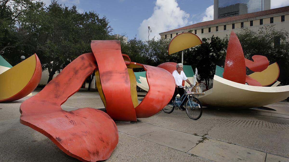 A man and his dog ride through “Dropped Bowl with Scattered Slices and Peels,” an Art in Public Places sculpture at the Miami-Dade County Government Center.