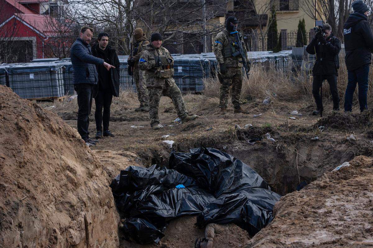 People stand next to a mass grave in Bucha, on the outskirts of Kyiv, Ukraine, on Monday, April 4. AP journalists saw dozens of bodies in Bucha, many of them shot at close range, and some with their hands tied behind them.