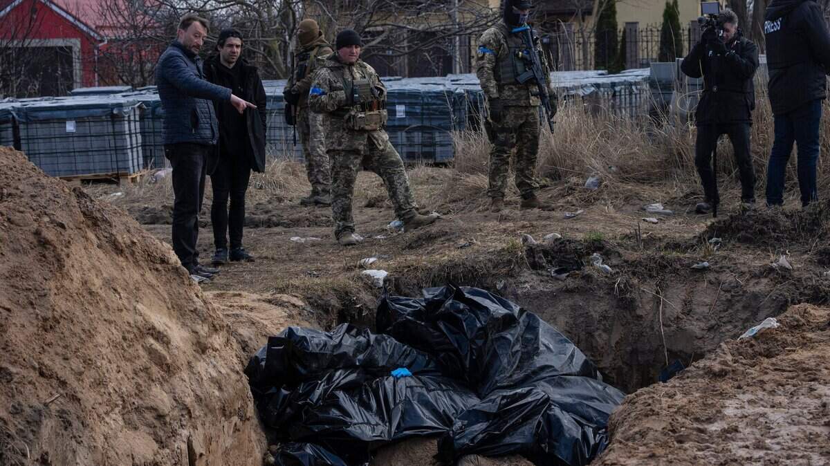 People stand next to a mass grave in Bucha, on the outskirts of Kyiv, Ukraine, on Monday, April 4. AP journalists saw dozens of bodies in Bucha, many of them shot at close range, and some with their hands tied behind them.