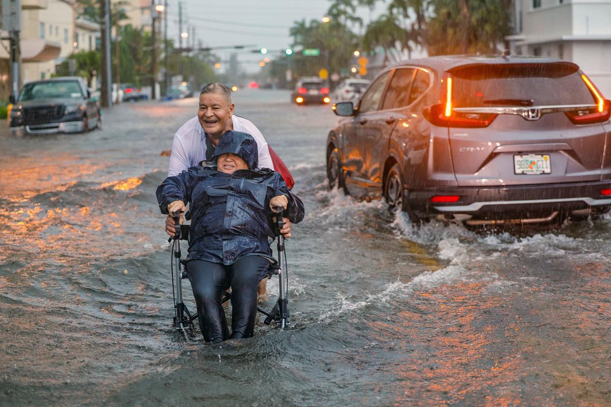 Victor Corone, 66, pushes his wife Maria Diaz, 64, in a wheelchair through more than a foot of flood water on 84th street in Miami Beach on Wednesday, June 12, 2024.