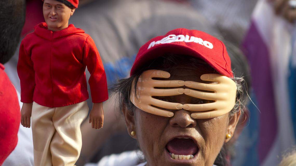 In this Friday, May 4, 2018 photo, a woman wearing a set of hands over her face holds up a doll of Venezuela's late President Hugo Chavez during an election campaign rally for current President Nicolas Maduro in the Catia neighborhood of Caracas, Venezuela. The hands represent 10 million votes the ruling party wants to reach in the presidential elections set for May 20. (AP Photo/Ariana Cubillos)