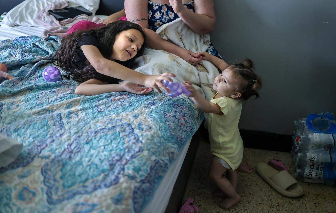 Itchel Perez, 1, right, plays her sister, Paola, left, while holding her mother's hand. The family of three are staying at Ernesto Motel after an attempt to self-deport stalled when their travel documents were taken at the border several years ago while seeking asylum in the United States on Thursday, April 2, 2026, in Miami, Florida.