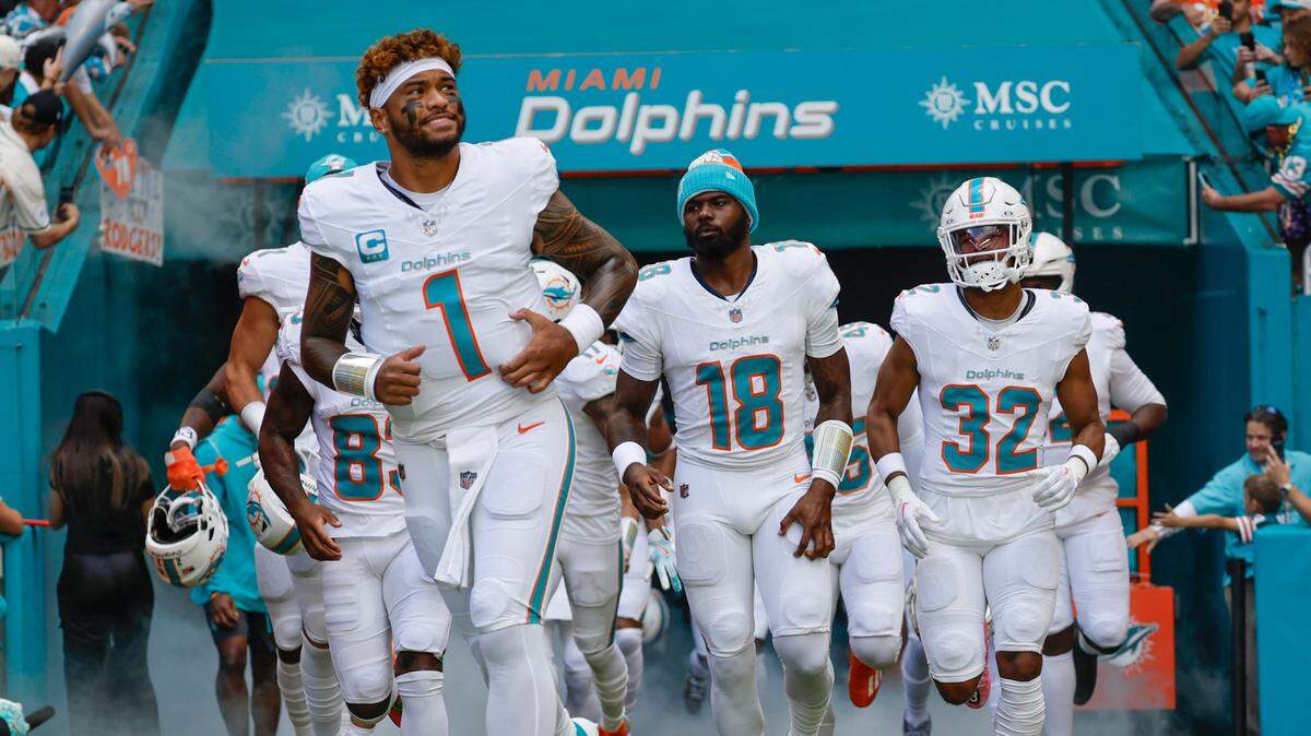 Los quarterbacks de los Miami Dolphins, Tua Tagovailoa (1) y Tyler Huntley (18), corren hacia el campo con sus compañeros de equipo antes del inicio de su partido de la NFL contra los New York Jets en el Hard Rock Stadium en Miami Gardens, Florida, el domingo 8 de diciembre de 2024.
