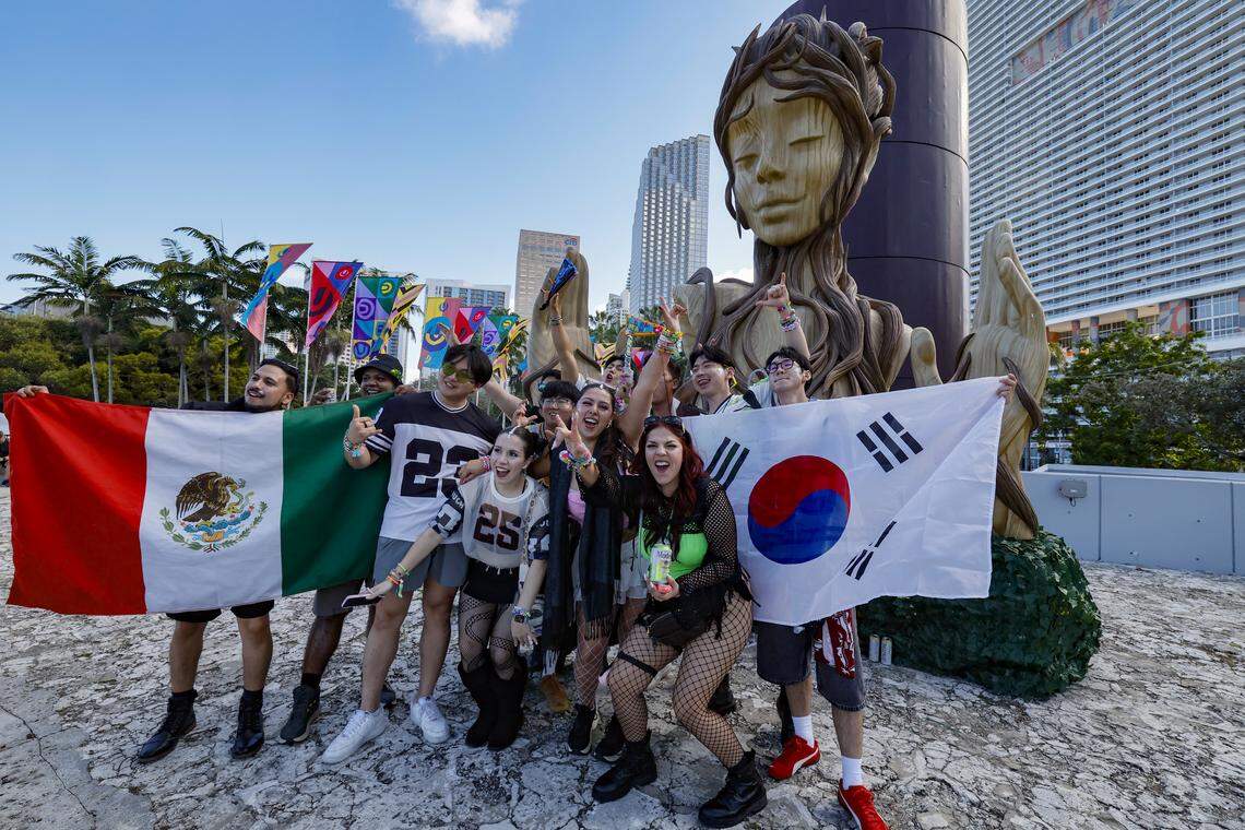 Attendees Javiera Shae, Fernanda Fuentes Paola, and Jihoan Minwo Gu, seen at center left to right, joins friends as they pose at a statue displayed at Bay Front Park during Ultra Music Festival in Miami, Florida, on Friday, March 27, 2026.