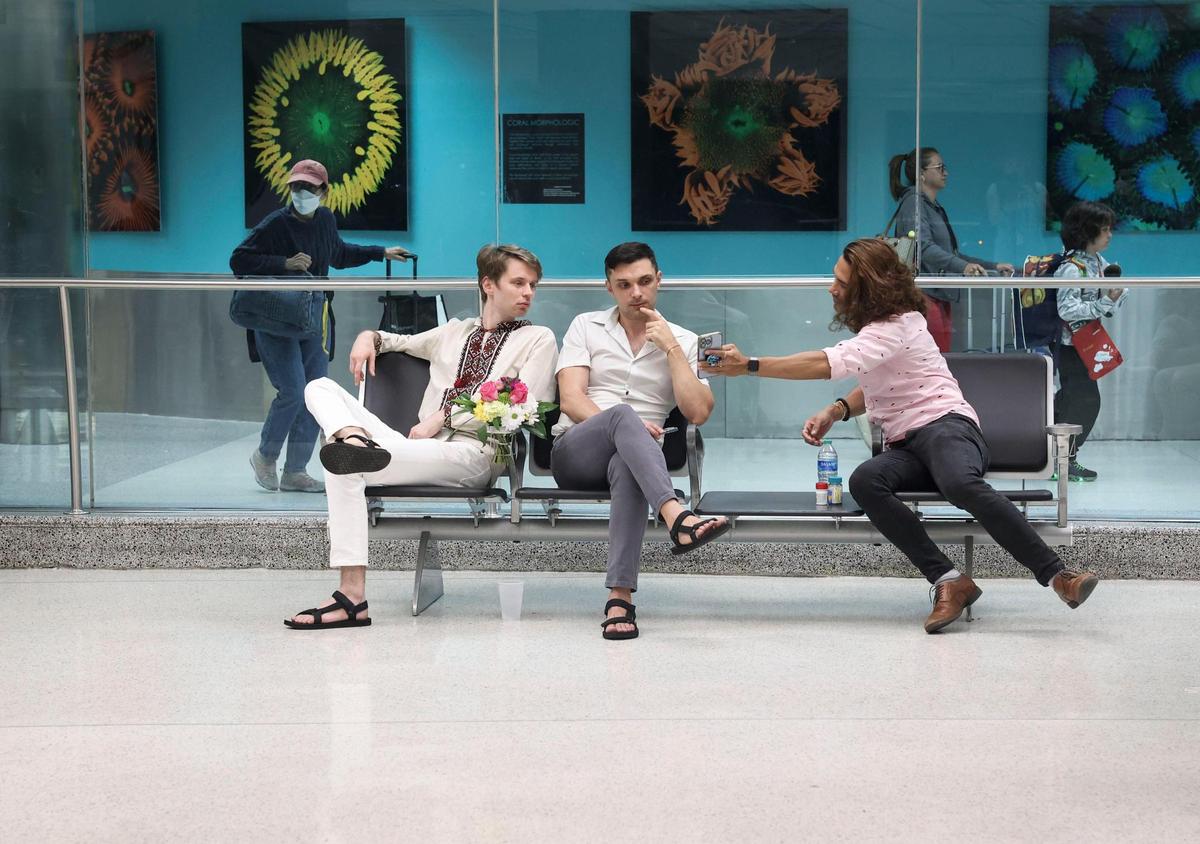 Roman Zhenzhirov, left, his husband, Roman Shyshkin, center, and friend Anthony Rojas wait for Zhenzhirov’s family while they go through customs on Tuesday, June 21, 2022, at Miami International Airport. The family got pulled aside for extra screening upon entering the country. Zhenzhirov’s family is a part of the Biden administration’s Uniting for Ukraine, which allowed Ukrainian citizens to come to the U.S. and stay with their families for up to two years.