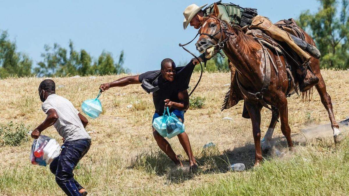 A border agent menaces a Haitian migrant at the Texas border, grabbing him and brandishing a whip.