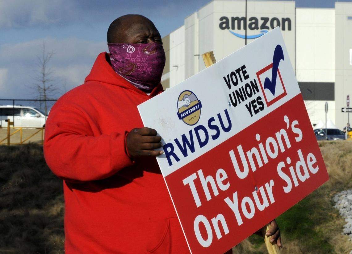 In this Feb. 9, 2021 file photo, Michael Foster of the Retail, Wholesale and Department Store Union holds a sign outside an Amazon facility where labor is trying to organize workers in Bessemer, Alabama.