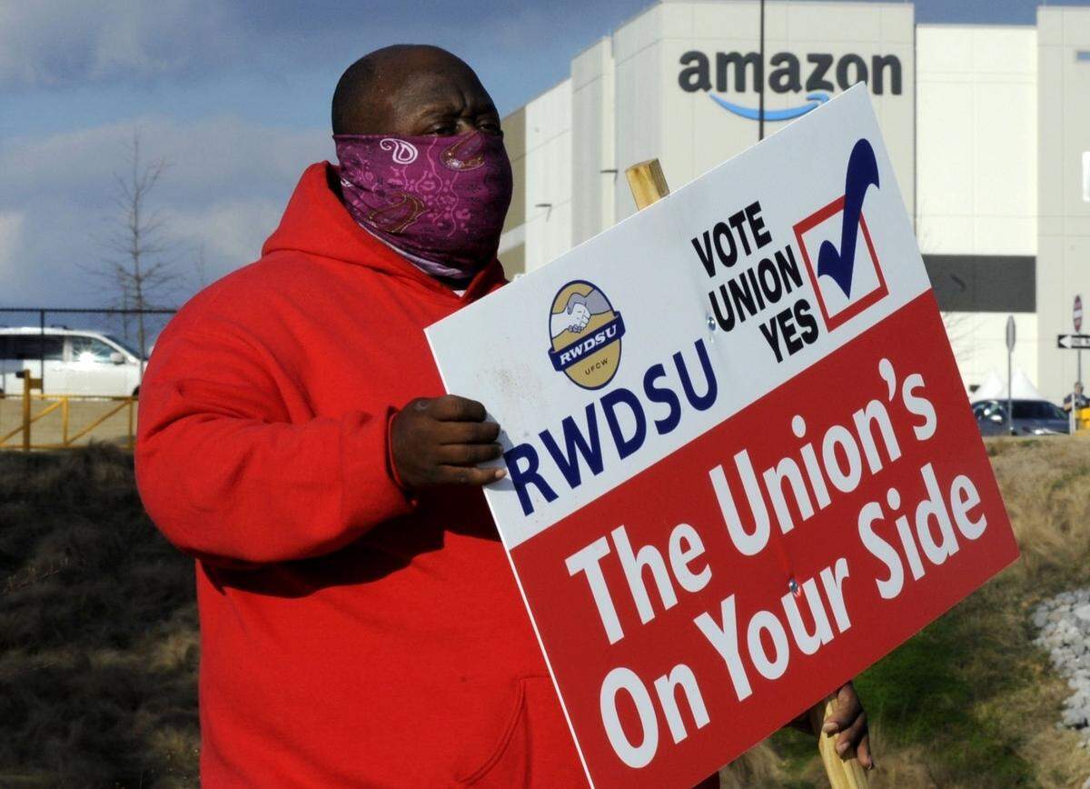 In this Feb. 9, 2021 file photo, Michael Foster of the Retail, Wholesale and Department Store Union holds a sign outside an Amazon facility where labor is trying to organize workers in Bessemer, Alabama.