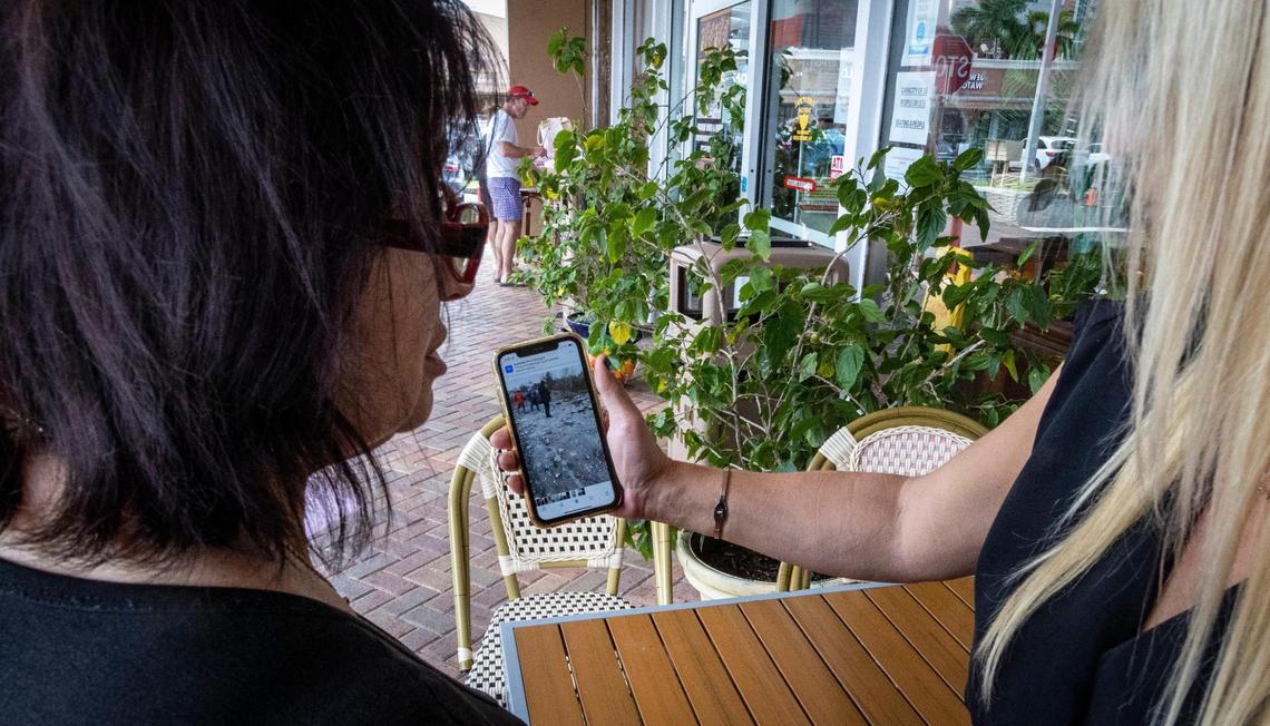 Olena Doronina, from Kherson, Ukraine, left, watches a video from Ukraine that her Russian friend Alexandra Ignatkina shows her on her cell phone in front of Matryoshka Deli in Sunny Isles.