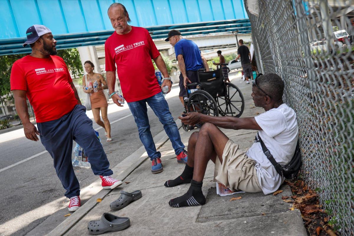Outreach worker Denny Baldonado, 40, left, and Homeless Trust Chairman Ron Book, center, walk through downtown and stop to speak with Juan Almeida, right, as they survey the area and offer services to unhoused individuals on the street on Thursday, Aug. 1, 2024, in Miami, Florida.