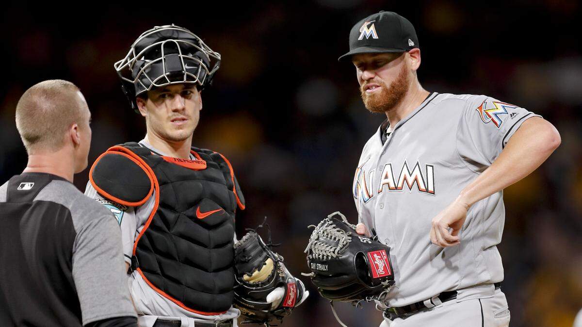 Miami Marlins starting pitcher Dan Straily, right, points to his side as team trainer Dustin Luepker, left, and catcher J.T. Realmuto visit him on the mound while he was pitching against the Pittsburgh Pirates in the fifth inning of a baseball game, Friday, Sept. 7, 2018, in Pittsburgh. Straily was removed from the game.