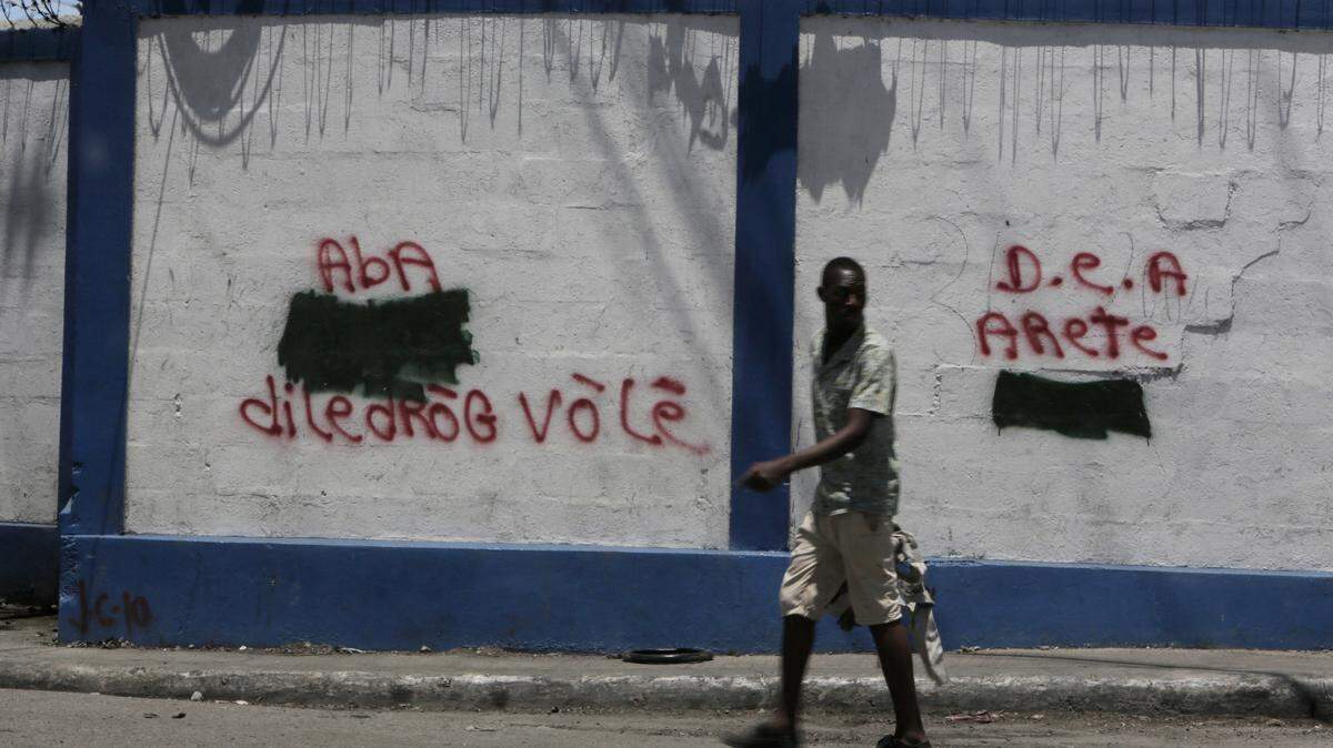 In this file photo, a man walks past the government port in Port-au-Prince, Haiti, where graffiti on the walls calls for the DEA to arrest someone for drug dealing.